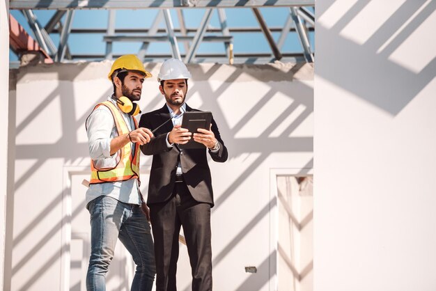 Ingeniero civil y gerente de trabajadores de la construcción con tableta digital y planos hablando y planeando sobre el sitio de construcción Concepto de trabajo en equipo de cooperación