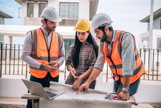 Ingeniero civil Trabajador de la construcción y arquitectos que usan cascos y chalecos de seguridad están trabajando juntos en el sitio de construcción construyendo una casa en concepto de trabajo en equipo de cooperación