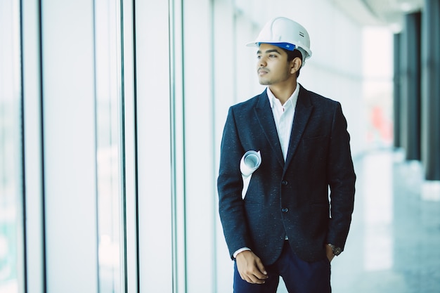 Ingeniero contratista de sitio masculino indio con casco con papel de impresión azul caminando en el sitio de construcción