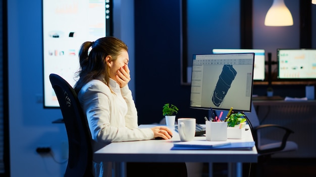 Ingeniero diseñador cansado analizando nuevo prototipo de modelo 3D de la planta bostezando trabajando horas extras. Trabajadora industrial estudiando la idea de la turbina en la pc que muestra el software cad en la pantalla del dispositivo