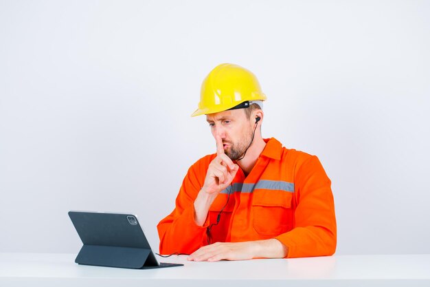 Ingeniero enojado está mostrando un gesto de silencio sosteniendo el dedo índice en los labios sobre fondo blanco.