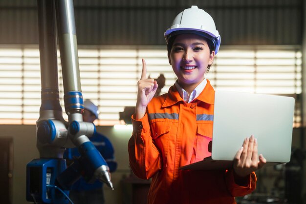 Ingeniero especialista asiático femenino y mantenimiento técnico inspeccionar el sistema de brazo de robot de relé con computadora portátil para controlar la calidad operar proceso trabajo industria pesada 40 fabricación fábrica inteligente