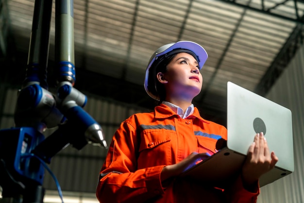 Ingeniero especialista asiático femenino y mantenimiento técnico inspeccionar el sistema de brazo de robot de relé con computadora portátil para controlar la calidad operar proceso trabajo industria pesada 40 fabricación fábrica inteligente