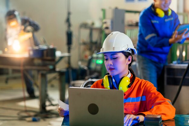 Ingeniero especialista asiático femenino y mantenimiento técnico inspeccionar el sistema de brazo de robot de relé con computadora portátil para controlar la calidad operar proceso trabajo industria pesada 40 fabricación fábrica inteligente