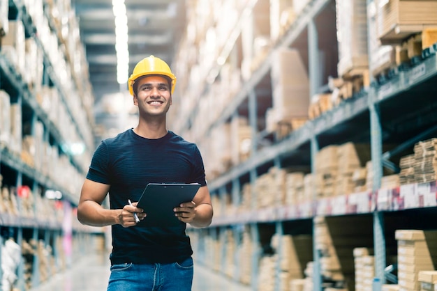 Ingeniero indio inteligente con casco de seguridad haciendo verificación de existencias y gestión de productos de existencias de cartón en el fondo del almacén de la fábrica