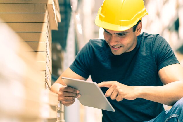 Ingeniero indio inteligente con casco de seguridad haciendo verificación de existencias y gestión de productos de existencias de cartón en el fondo del almacén de la fábrica