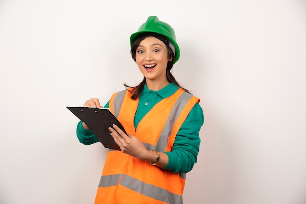 Ingeniero industrial femenino positivo en uniforme con portapapeles sobre fondo blanco.