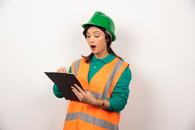 Ingeniero industrial mujer sorprendido en uniforme con portapapeles sobre fondo blanco.