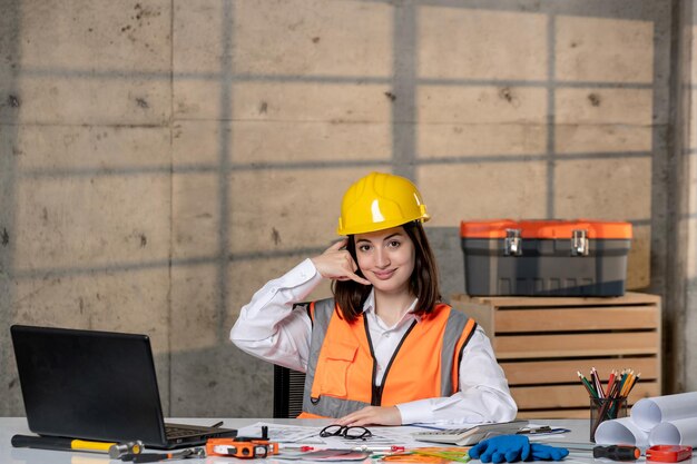 Ingeniero inteligente joven linda chica morena trabajador civil en casco y chaleco haciendo señal de llamada