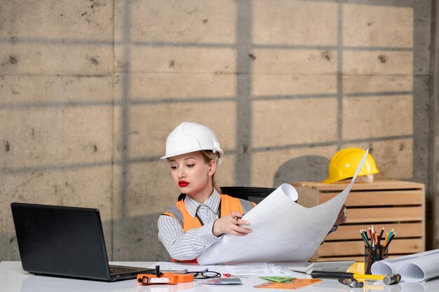 Ingeniero inteligente joven linda chica rubia trabajador civil en casco y chaleco mirando proyecto