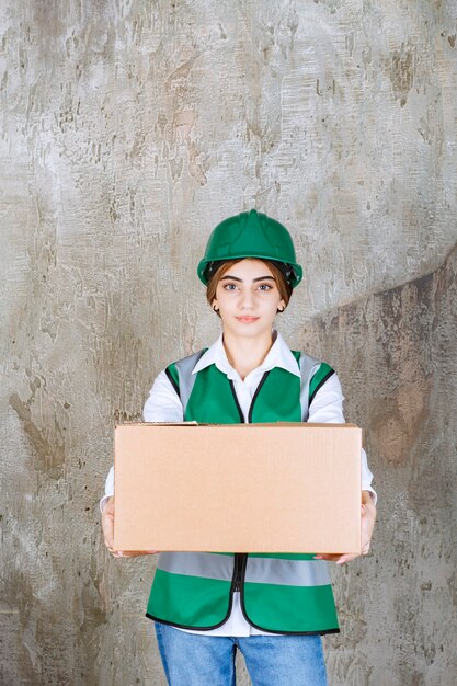 Ingeniero joven en chaleco verde y casco con caja de papel