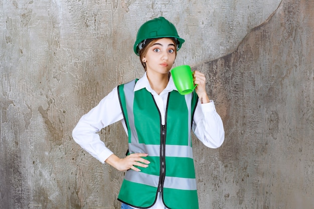 Foto gratuita ingeniero joven vistiendo un chaleco verde y sosteniendo una taza de café