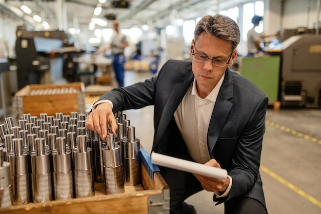 Ingeniero masculino leyendo documentos mientras verifica la calidad de la barra de acero fabricada en un edificio industrial