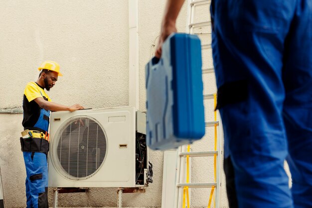 Ingeniero que llega al lugar para ayudar al aprendiz a reparar las bobinas eléctricas rotas en el aire acondicionado externo dañado Técnicos encargados de evitar las averías de las piezas internas asegurando la reparación oportuna