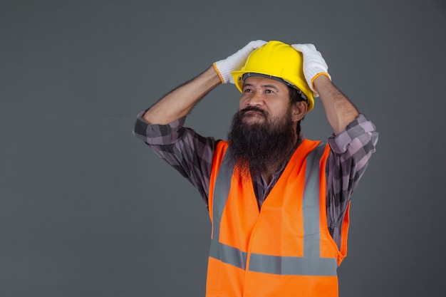 Foto gratuita un ingeniero que llevaba un casco amarillo con guantes blancos mostró un gesto en un gris.