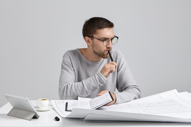 Ingeniero de sexo masculino pensativo serio mantiene la pluma y el cuaderno en las manos, planes de reunión,