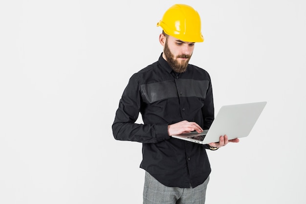 Ingeniero de sexo masculino que desgasta el casco usando la computadora portátil contra el fondo blanco