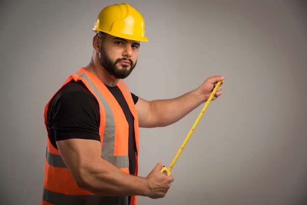 Ingeniero en uniforme naranja y casco amarillo con regla.