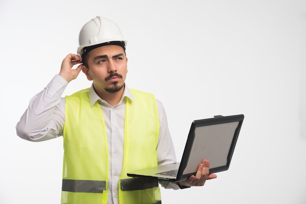 Ingeniero en uniforme sosteniendo una computadora portátil y pensando.