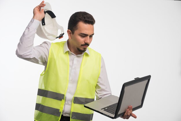 Ingeniero en uniforme sosteniendo una computadora portátil y sacando su casco.