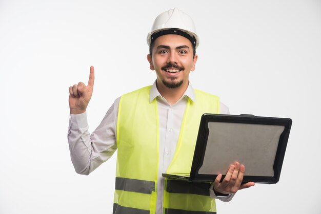 Ingeniero en uniforme sosteniendo una computadora portátil y teniendo una idea.