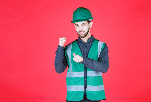 Ingeniero en uniforme verde y casco apuntando hacia atrás.