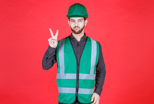 Ingeniero en uniforme verde y casco enviando paz y amistad.