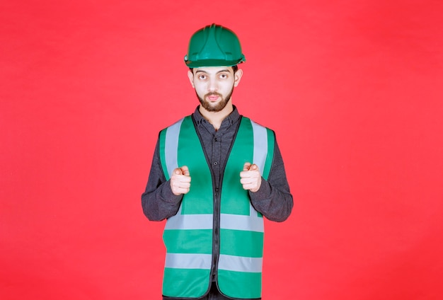 Ingeniero en uniforme verde y casco notando a la persona de adelante.