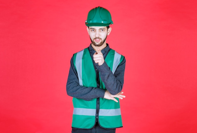Foto gratuita ingeniero en uniforme verde y casco notando a la persona de adelante.