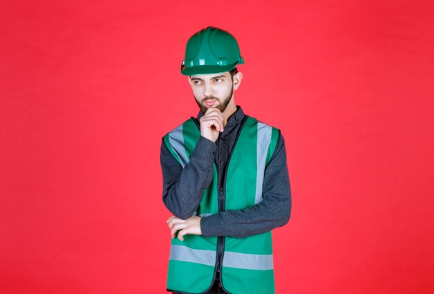 Ingeniero en uniforme verde y casco pensando y planificando.