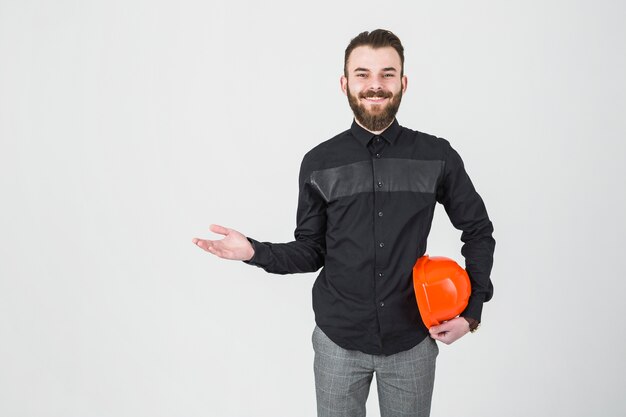 Un ingeniero varón sonriente que sostiene el sombrero duro que se encoge de hombros