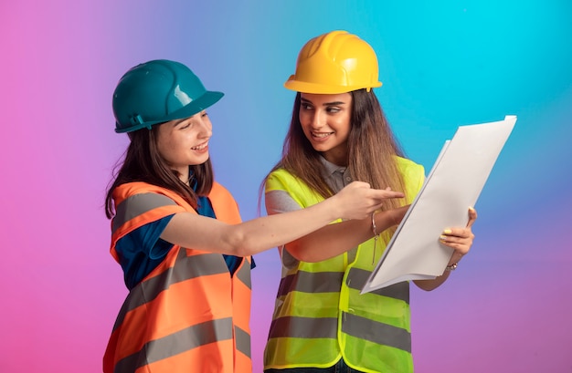 Ingenieros de construcción femeninos trabajando juntos y discutiendo el plan del proyecto sobre fondo de colores.