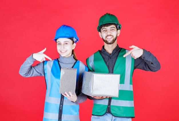 Ingenieros masculinos y femeninos con casco con cajas de regalo plateadas.