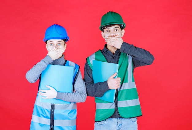 Ingenieros masculinos y femeninos con casco sosteniendo carpetas de informes y parece asustado y aterrorizado.