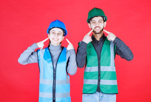 Ingenieros masculinos y femeninos con cascos apuntando a sí mismos.