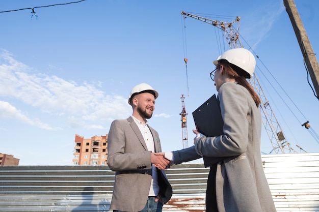 Ingenieros sonrientes que sacuden las manos en el emplazamiento de la obra para el proyecto arquitectónico