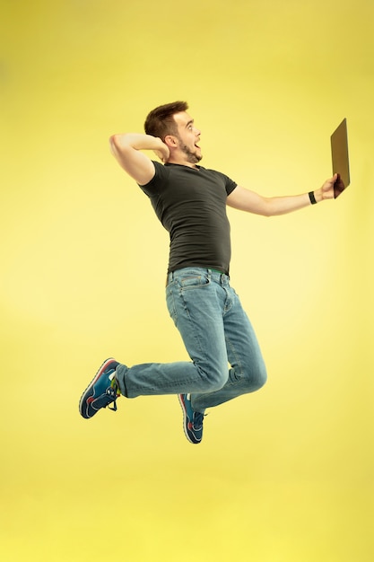 Ingrávido. Retrato de cuerpo entero de hombre feliz saltando con gadgets aislados sobre fondo amarillo