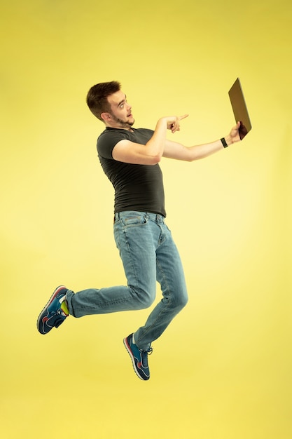 Ingrávido. Retrato de cuerpo entero de hombre feliz saltando con gadgets aislados sobre fondo amarillo