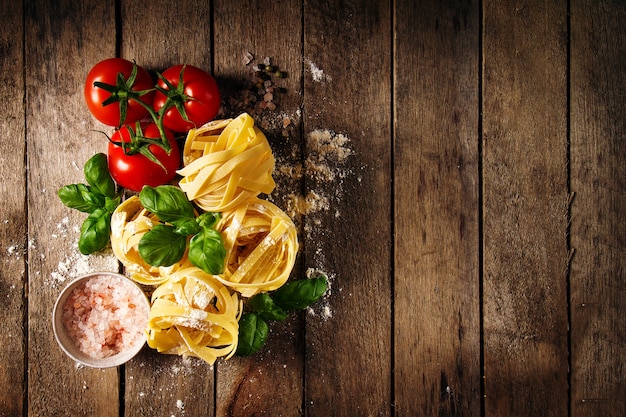 Ingredientes coloridos frescos sabrosos para cocinar las pastas Tagliatelle con albahaca fresca y tomates. Vista superior. Fondo De Madera De La Tabla.