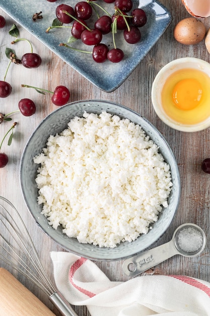 Ingredientes para hacer albóndigas de requesón con cerezas Requesón harina de huevo y cerezas frescas en una mesa de madera Vertical