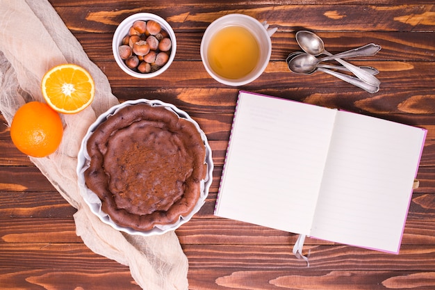 Ingredientes para pastel de chocolate con cucharas y diario blanco sobre el escritorio de madera