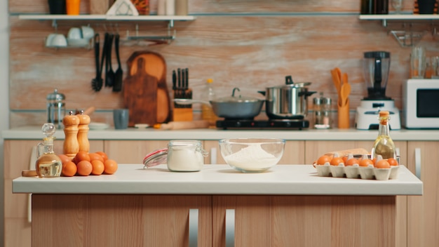 Ingredientes de pastelería para pasteles caseros y pan en cocina vacía. Comedor moderno equipado con utensilios listos para cocinar con harina de trigo en un tazón de vidrio y huevos frescos en la mesa