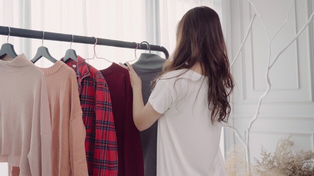 Inicio vestuario o tienda de vestuario vestuario. Mujer joven asiática que elige su ropa del equipo de la moda