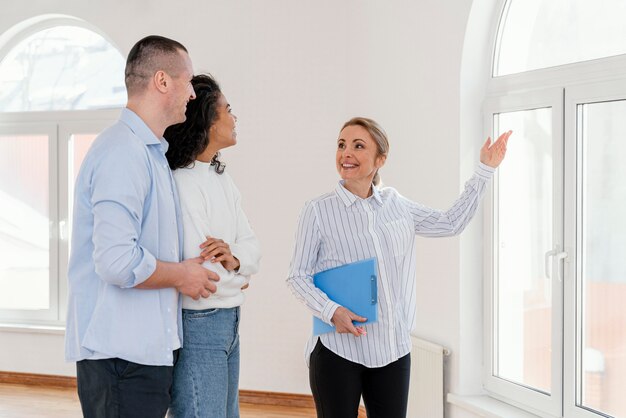 Inmobiliaria mujer sonriente mostrando casa vacía a pareja joven