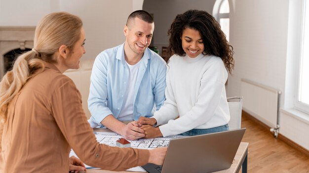 Inmobiliaria sonriente mostrando nueva casa a la pareja en la computadora portátil