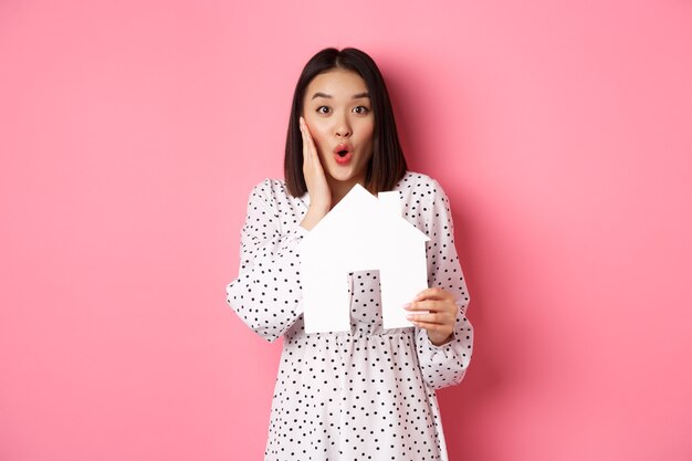 Inmobiliaria sorprendida y sorprendida mujer asiática mirando a la cámara diciendo wow y mostrando la casa de papel mo ...