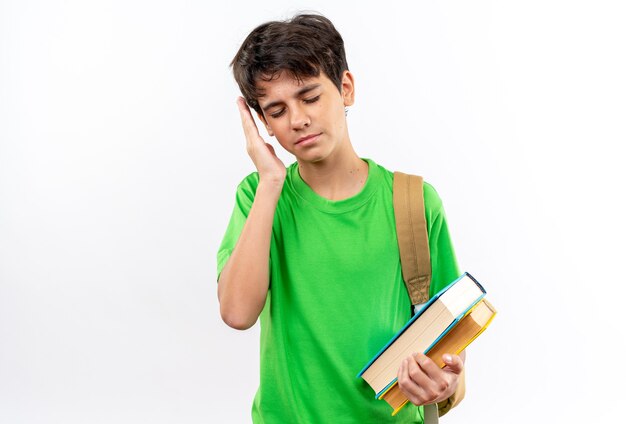 Insatisfecho con los ojos cerrados joven escolar con mochila sosteniendo libros