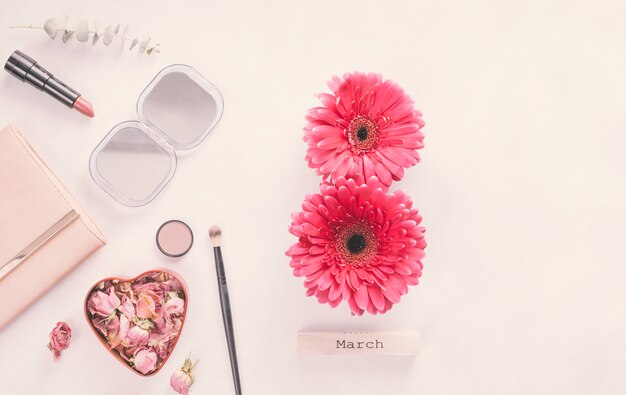 Inscripción del 8 de marzo de flores de gerbera con cosméticos en mesa.