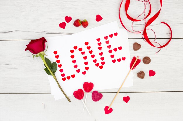Inscripción de amor en papel cerca de corazones de chocolate, cinta y flor.