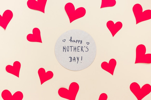 Inscripción del día de las madres felices con corazones de papel en la mesa